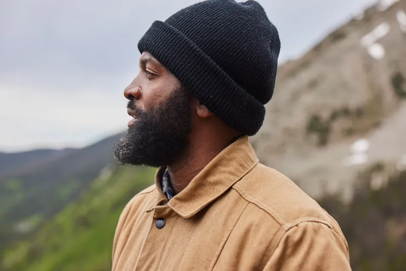 Baratunde Thurston in a beanie and work jacket, looking out over mountains